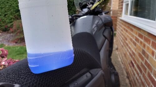 car coolant sitting on motorcycle seat, blue car coolant in bottle on motorcycle
